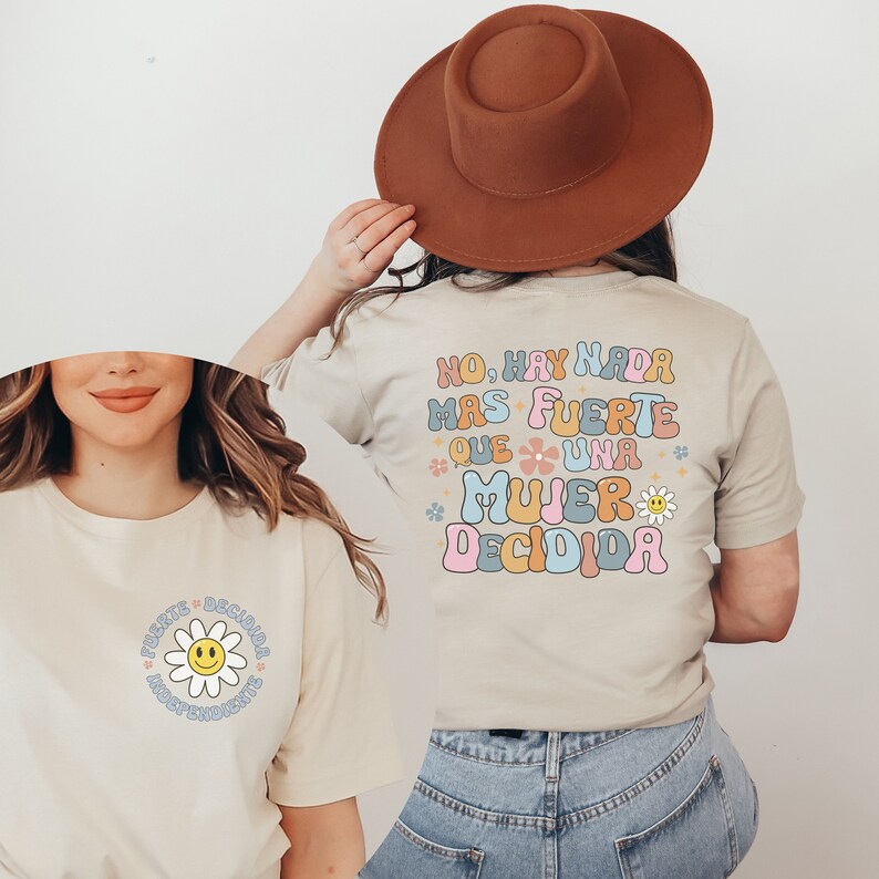 Pu&ograve; includere: Due t-shirt beige con un design grafico che presenta una margherita e il testo "No, hay nada mas fuerte que una mujer decidida".