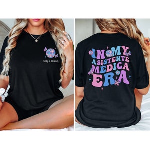May include: Black t-shirt with a disco ball and butterflies on the front and the text "In My Asistente Medica Era" with butterflies and stars on the back.