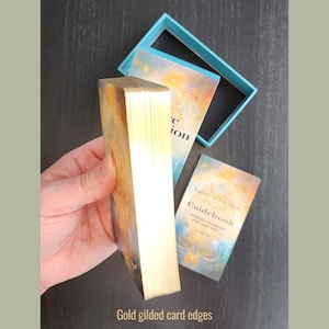 Close-up of gold gilded edges on Nature & Intuition Oracle Deck cards and the open two-piece box behind.