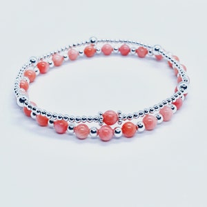 May include: A delicate bracelet featuring alternating silver and pink beads. The bracelet is made up of two strands of beads, one with silver beads and the other with pink beads.