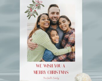May include: A rectangular holiday card featuring a photograph of a family of four embracing. Above the photo is a green mistletoe illustration with a red bow. Below the photo, the red text reads: WE WISH YOU A MERRY CHRISTMAS The Smith Family.