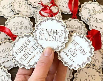 May include: Twenty-five wooden ornaments with white text on a white background. Each ornament features a different name of Jesus with a corresponding Bible verse. The ornaments are decorated with a simple leaf design around the edge.