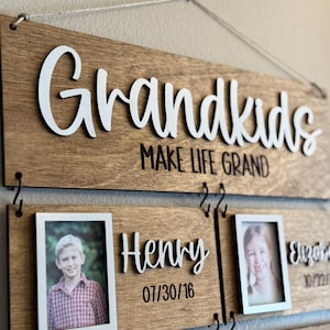 Op de afbeelding: Houten bord met het woord "Grandkids" in het wit, met de zin "MAKE LIFE GRAND" eronder. Inclusief fotolijsten met de namen "Henry" en "Elizabeth" en hun geboortedata.