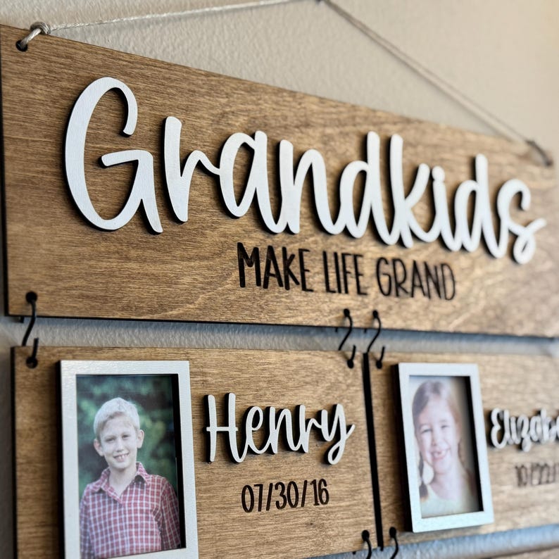 Op de afbeelding: Houten bord met het woord "Grandkids" in het wit, met de zin "MAKE LIFE GRAND" eronder. Inclusief fotolijsten met de namen "Henry" en "Elizabeth" en hun geboortedata.