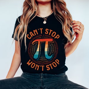 May include: A black t-shirt with a rainbow colored graphic of the mathematical symbol pi, surrounded by the digits of pi. The text "CAN'T STOP WON'T STOP" is printed below the graphic.