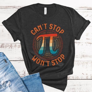 May include: A dark gray t-shirt with a vintage-style graphic of the mathematical constant pi. The graphic features a rainbow color scheme and the text "CAN'T STOP WON'T STOP".