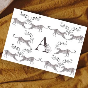 Puede incluir: Una tarjeta blanca con una letra A negra en el centro rodeada de animales de estampado de leopardo blanco y negro. Los animales están dispuestos en un círculo alrededor de la letra A.