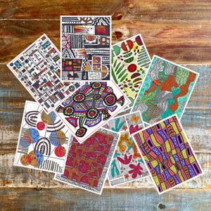 May include: A collection of colorful abstract art prints. Each print features unique geometric and organic designs in various colors, including red, blue, yellow, and green. The prints are arranged on a wooden surface.