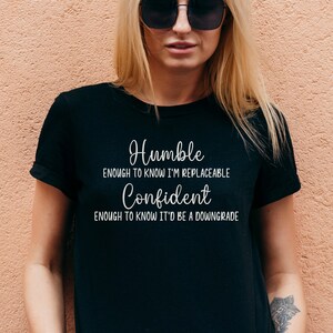 May include: Black t-shirt with white text that reads "Humble enough to know I'm replaceable. Confident enough to know it'd be a downgrade."