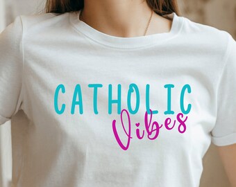 Peut inclure: T-shirt blanc avec le texte "CATHOLIC vibes" en lettres turquoise et rose.