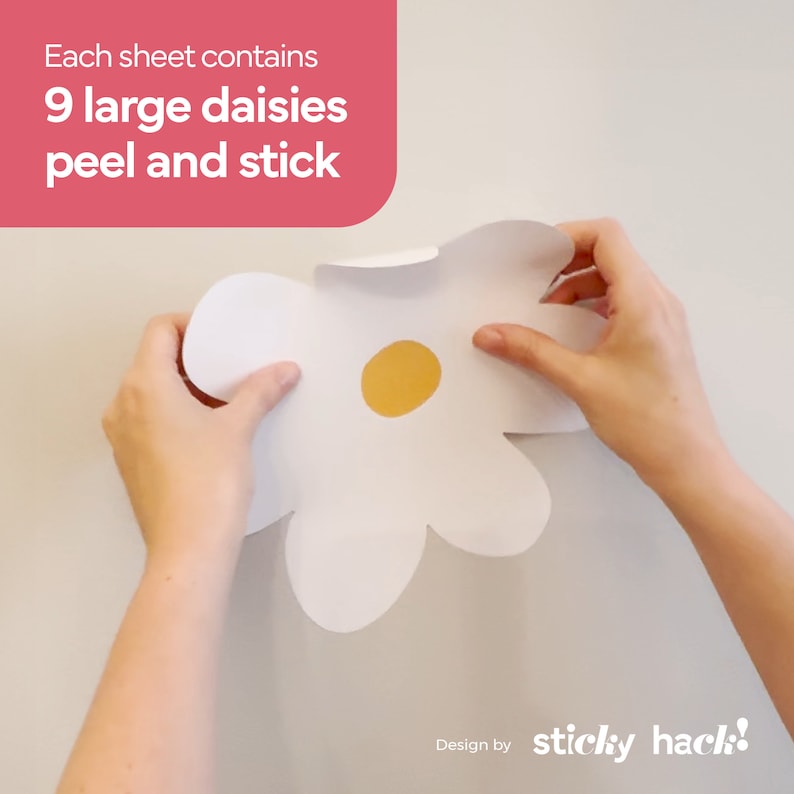 May include: A large white daisy peel and stick decal with a yellow centre is held up against a white wall. The text in the upper left corner reads, "Each sheet contains 9 large daisies peel and stick."
