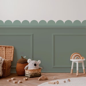 Peut inclure: Une chambre d'enfant avec un mur vert et une bordure festonnée. Un panier en osier, un récipient tissé et un panier avec une peluche koala sont posés sur le sol en bois. Un petit tabouret blanc supporte un arc-en-ciel en bois. Des blocs de bois et un tapis complètent le décor.