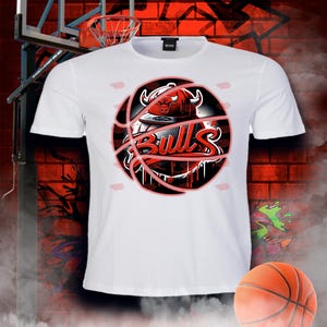 May include: White t-shirt featuring a red and black basketball graphic with the word "Bulls" and a bull's head wearing a hat.