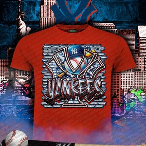 May include: Red t-shirt featuring a graphic design of the New York Yankees logo, baseball, and a baseball bat. The design incorporates brick-like elements and graffiti-style lettering. The background includes cityscapes and the Statue of Liberty.