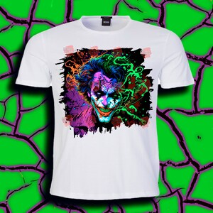 May include: White t-shirt with a colorful graphic print of the Joker's face. The graphic is in a grunge style with splashes of color and a black outline.