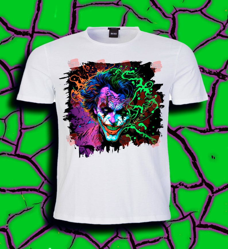 May include: White t-shirt with a colorful graphic print of the Joker's face. The graphic is in a grunge style with splashes of color and a black outline.