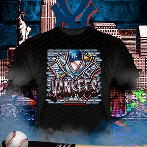 May include: Black t-shirt featuring a graffiti-style design with the word "Yankees" in red and white, along with a baseball and a baseball bat. The background includes a cityscape and the Yankees logo.