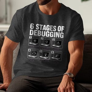 Dark grey t-shirt with "6 Stages of Debugging" graphic and laptop illustrations.