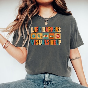 Peut inclure: Un t-shirt gris anthracite à manches courtes avec le texte "LIFE HAPPENS" au-dessus de cinq icônes carrées colorées représentant un smiley, une personne à un ordinateur, des mains en cœur, une personne au lit et un panneau stop, avec "VISUALS HELP" en dessous.