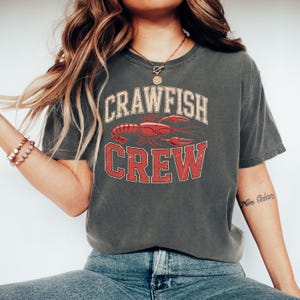 May include: A grey t-shirt with a vintage-style graphic of a crawfish and the text "Crawfish Crew".