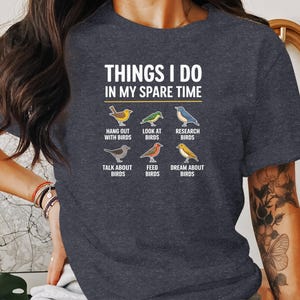 May include: A dark blue t-shirt with the text "Things I do in my spare time" and a graphic of six different birds with text describing what the person does with the birds. The text includes "Hang out with birds", "Look at birds", "Research birds", "Talk about birds", "Feed birds", and "Dream about birds".