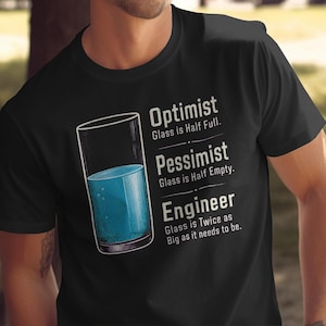 May include: A black short-sleeved t-shirt featuring a graphic of a glass filled with blue liquid. The text reads: Optimist Glass is Half Full. Pessimist Glass is Half Empty. Engineer Glass is Twice as Big as it needs to be.