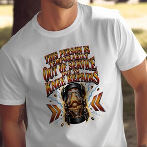 May include: A white short-sleeved t-shirt featuring a graphic print with the text "THIS PERSON IS TEMPORARILY OUT OF SERVICE DUE TO KNEE REPAIRS" in orange and yellow letters above an illustration of a mechanical knee brace with blue lightning.