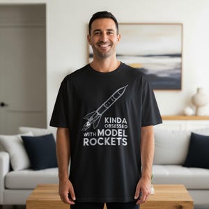 May include: Black t-shirt with a white graphic of a rocket and the text "KINDA OBSESSED WITH MODEL ROCKETS." The shirt is a short-sleeved crew neck.