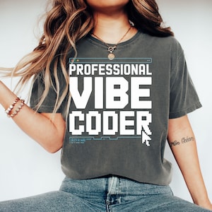 Può includere: Una maglietta grigia con la scritta bianca "PROFESSIONAL VIBE CODER" a blocchi. Il design include una cornice di finestra del computer e un cursore del mouse pixelato. La maglietta è di stile casual.