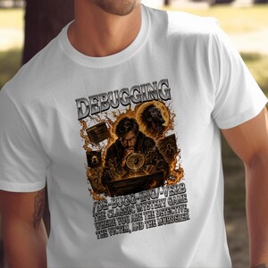 Op de afbeelding: Een wit t-shirt met een grafische print van een persoon die door een vergrootglas naar een computerscherm kijkt. De tekst luidt DEBUGGING /DE-BUGG-ING/-VERB THE CLASSIC MYSTERY GAME WHERE YOU ARE THE DETECTIVE, THE VICTIM, AND THE MURDERER.