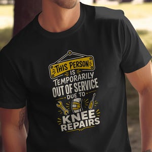 May include: A black short-sleeved t-shirt featuring a yellow and white graphic print that reads: THIS PERSON IS TEMPORARILY OUT OF SERVICE DUE TO KNEE REPAIRS. The design includes illustrations of a wrench, a screwdriver, and a bandaged knee.