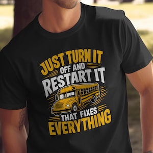 Könnte beinhalten: Ein schwarzes T-Shirt mit kurzen Ärmeln und einer gelben Schulbus-Grafik in der Mitte. Der Text JUST TURN IT OFF AND RESTART IT THAT FIXES EVERYTHING ist in gelben und weißen Blockbuchstaben um die Bus-Illustration angeordnet.