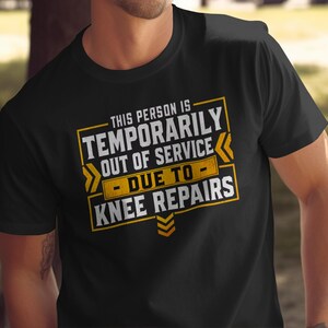 May include: A black short-sleeved t-shirt featuring a graphic design with yellow and white text that reads: THIS PERSON IS TEMPORARILY OUT OF SERVICE - DUE TO - KNEE REPAIRS, framed by yellow rectangular borders and chevron arrow accents.