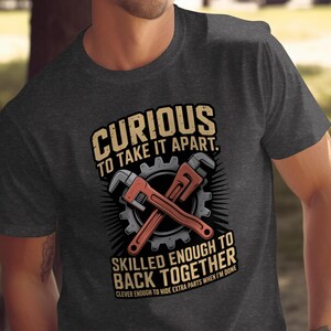 May include: Dark gray t-shirt with a graphic featuring crossed wrenches, a gear, and text that reads "Curious to take it apart. Skilled enough to back together. Clever enough to hide extra parts when I'm done."