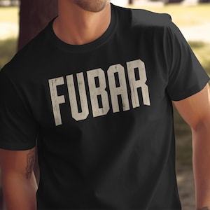 Puede incluir: Una camiseta negra de manga corta con la palabra FUBAR impresa en letras grandes de bloque color blanco roto con un aspecto desgastado en el pecho. La prenda tiene un cuello redondo y un corte estándar con tipografía texturizada.