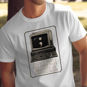 Könnte beinhalten: Ein weißes kurzärmeliges T-Shirt mit einer Grafik eines alten Computermonitors, auf dessen Bildschirm ein Semikolon zu sehen ist. Unter dem Computer steht der Text: DIDN'T SLEEP FOR TWO DAYS BECAUSE OF A SEMICOLON, alles in einem dünnen Rahmen.