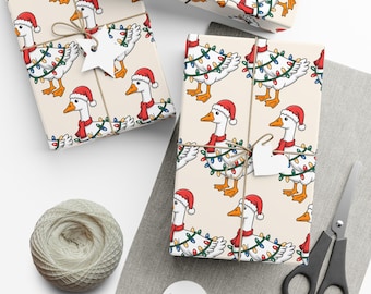 May include: Christmas-themed gift wrap featuring a repeating pattern of cartoon geese wearing Santa hats and scarves, adorned with string lights. The gifts are tied with twine and have blank star-shaped tags. A spool of twine and scissors are also visible.