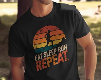 May include: Black t-shirt with a retro design featuring a runner silhouetted against a sunset. The text "EAT SLEEP RUN REPEAT" is printed in orange and white. The shirt is made of a soft material.