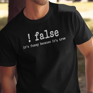 May include: A black short-sleeved t-shirt featuring white text printed on the chest. The text reads ! false in a large font, with the smaller text it's funny because it's true positioned directly underneath in a typewriter-style font.