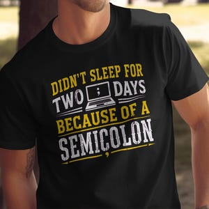 Puede incluir: Una camiseta negra de manga corta con un estampado gráfico que incluye el texto DIDN'T SLEEP FOR TWO DAYS BECAUSE OF A SEMICOLON. El diseño muestra un icono de portátil con un punto y coma en la pantalla, en letras amarillas y blancas.