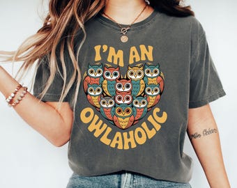 May include: Dark grey t-shirt with a heart-shaped design of colorful owls. The text "I'M AN OWLAHOLIC" is printed in yellow. The owls have blue, orange, and yellow details.