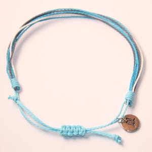 May include: A light blue, white, and gray braided bracelet with a silver charm. The charm has the letter "M" on it.