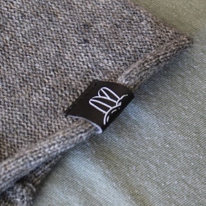 Peut inclure: Un bonnet en tricot gris avec un patch en cuir noir représentant un lapin blanc.