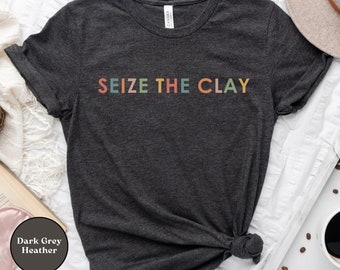 May include: A dark grey heather t-shirt with the text "SEIZE THE CLAY" in rainbow colors.