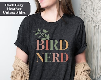 May include: A dark grey heather unisex t-shirt with the text "BIRD NERD" in colorful letters. A small bird is perched on a branch with leaves above the text.