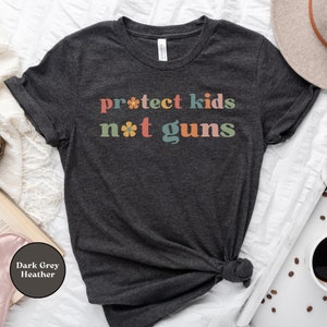 May include: Dark grey heather t-shirt with the text "protect kids not guns" in colorful retro font with flower accents.