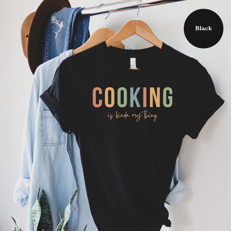 May include: Black t-shirt with the text "COOKING is kinda my thing" in colorful letters.