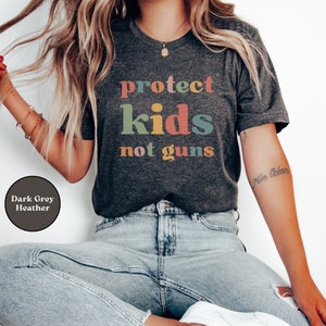 May include: A dark grey heather t-shirt with the text "protect kids not guns" in colorful letters.