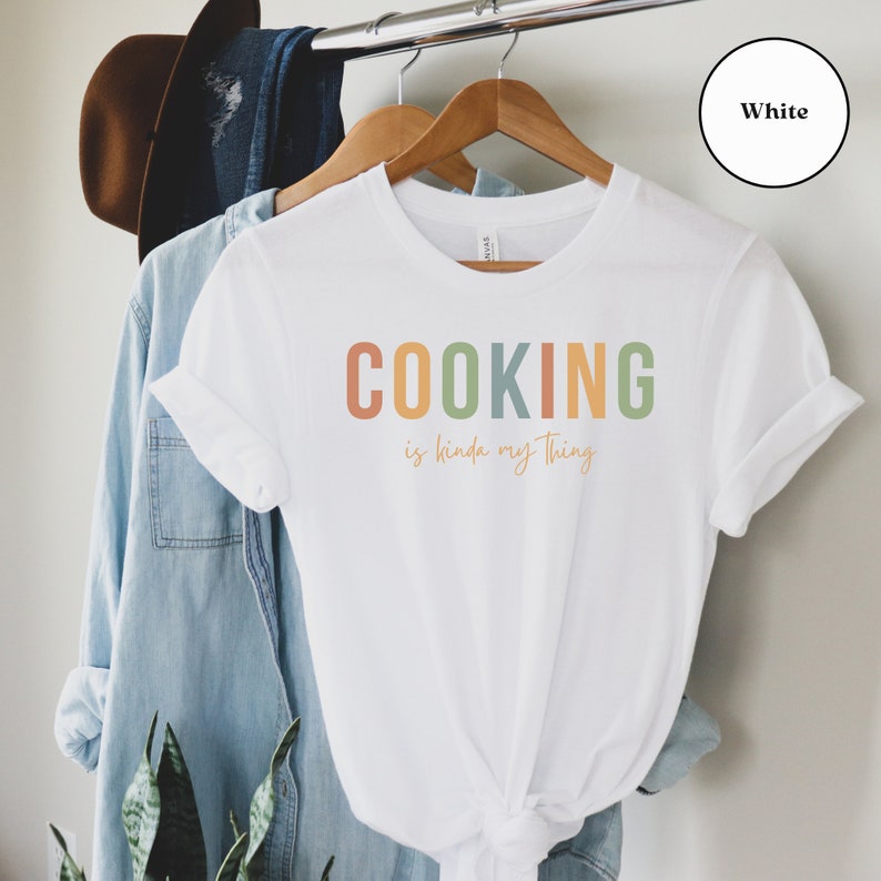 May include: White t-shirt with the text "COOKING is kinda my thing" in rainbow colors.