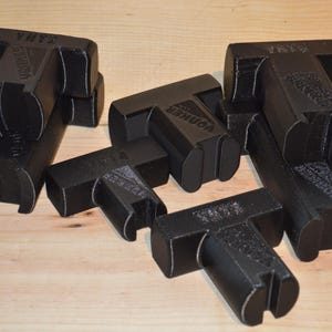 Peut inclure: Cinq équerres d'angle en plastique noir avec le mot "Corner" imprimé dessus. Les équerres sont empilées les unes sur les autres.